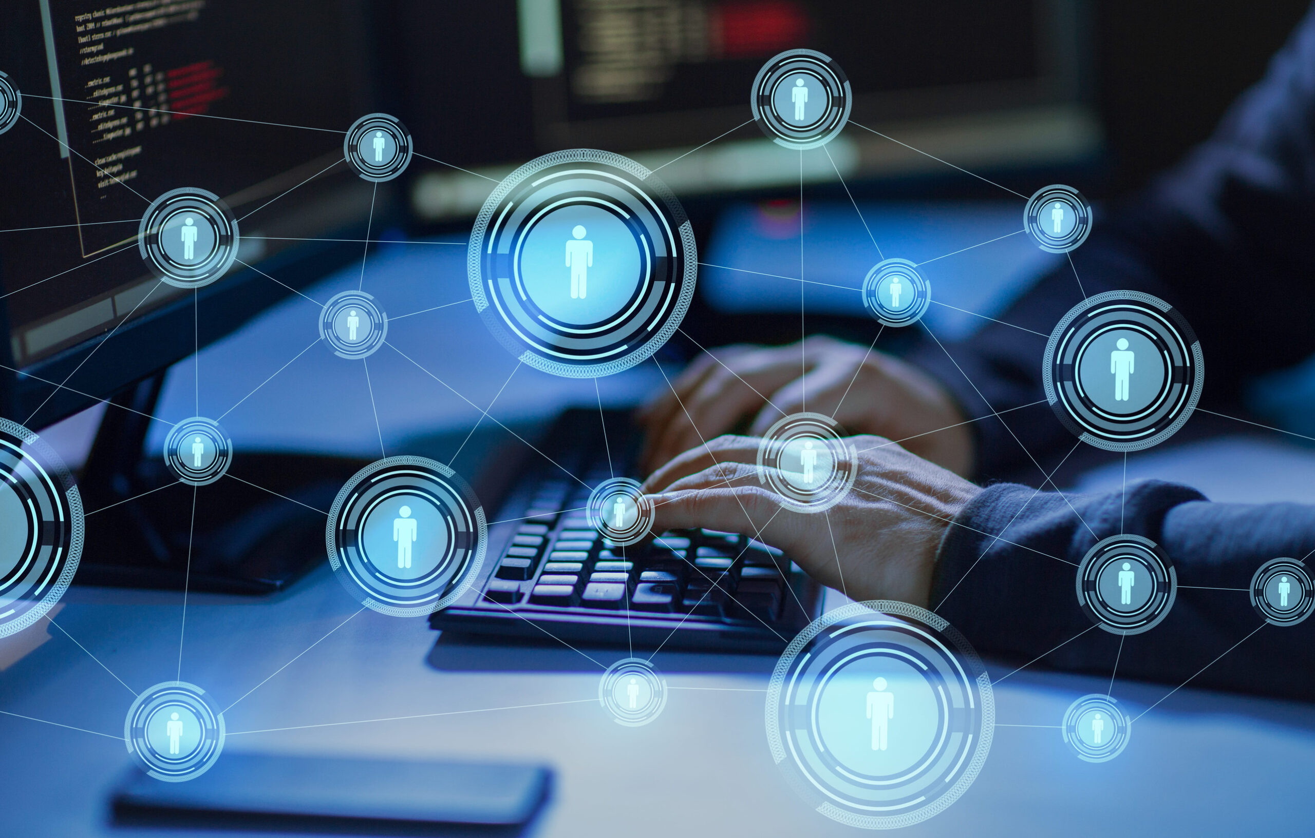 Person typing at a computer keyboard in a dim office, overlaid with glowing blue network icons showing connected user symbols across multiple nodes and screens.