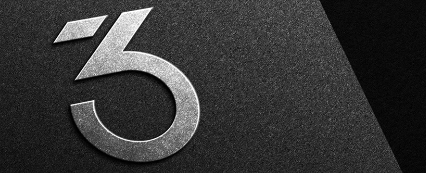 **Alt text:** Close-up of a metallic “3” logo mounted on a textured dark surface, featuring a sleek, modern design with a brushed metal finish.