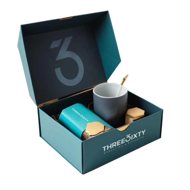 **Alt text:** Teal branded gift box with “THREE SIXTY Marketing & Branding” logo, containing a teal tumbler, a gray mug with a gold spoon, and small gold-accented items, arranged neatly inside.
